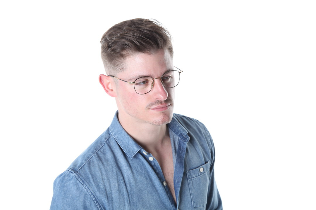 A man with glasses wearing a denim shirt poses against a white background.