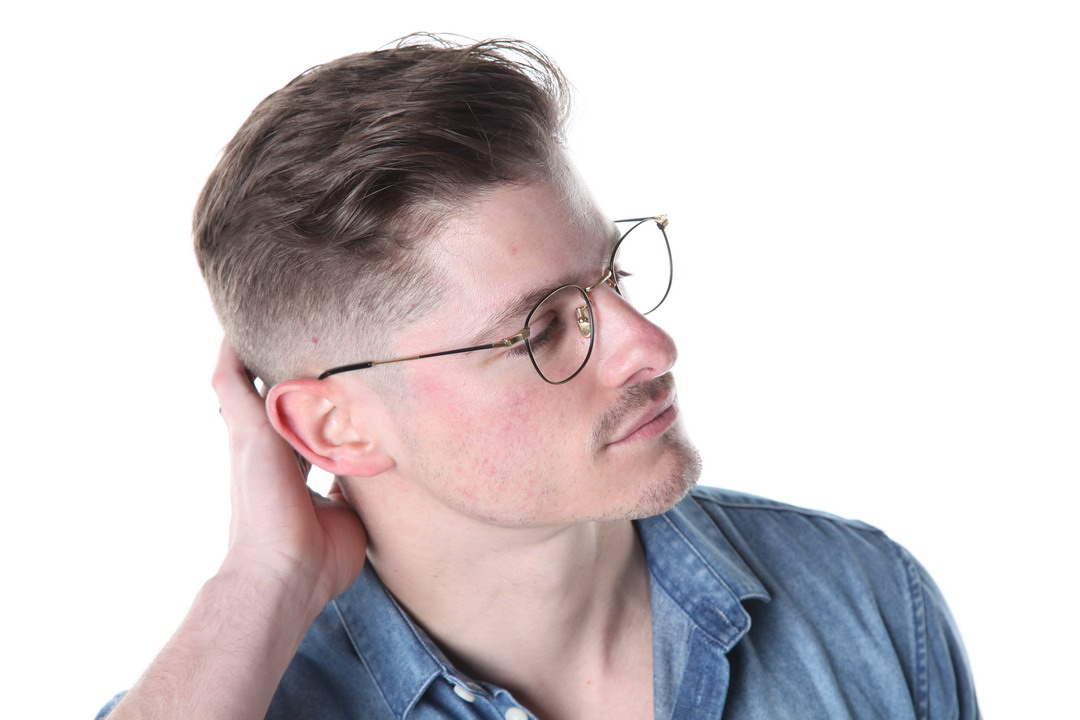 A man with glasses wearing a denim shirt looking to the side.